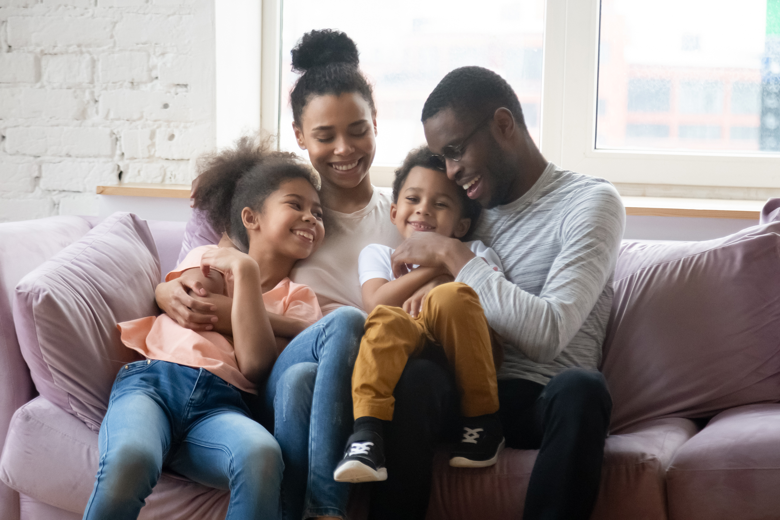 Happy african American young family with little kids sit on comfortable couch relax hug and cuddle in living room, smiling biracial parents enjoy weekend with small children, rest on sofa together